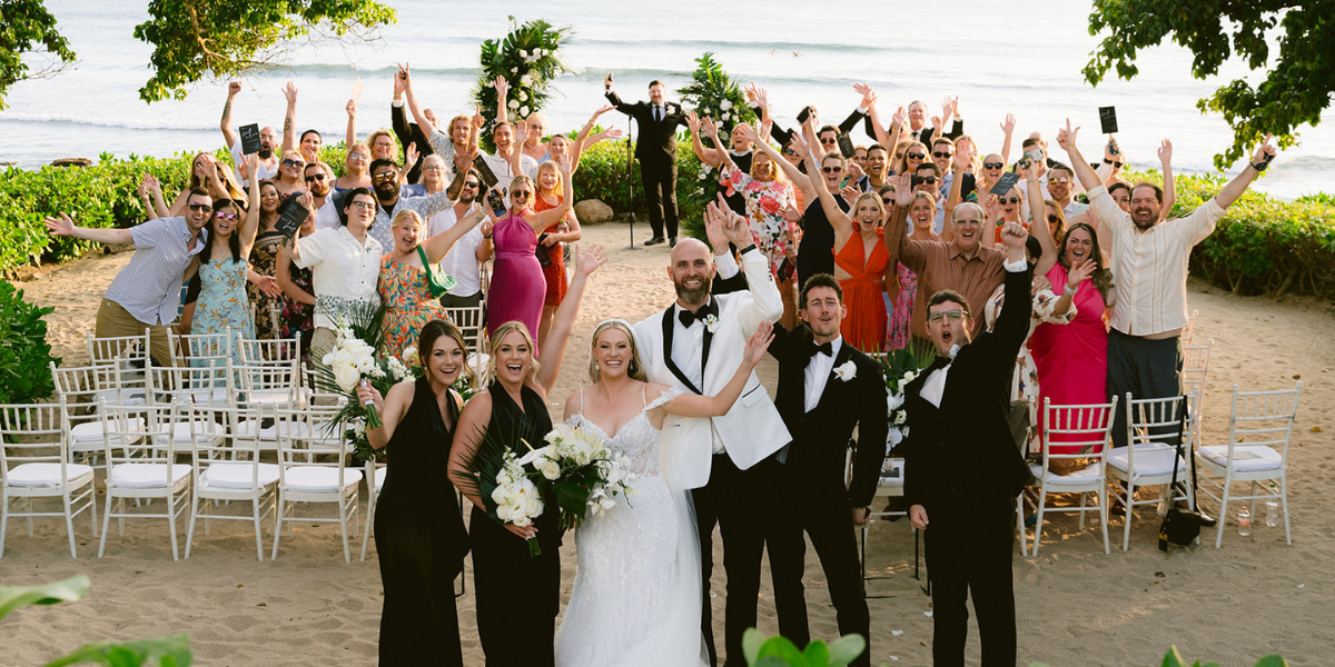 Bride and groom celebrating with cheering wedding party and guests on a Caribbean beach, ideal for affordable destination wedding planning